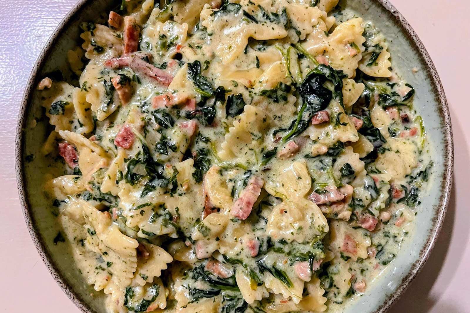 A rustic bowl of creamy farfalle pasta with wilted spinach