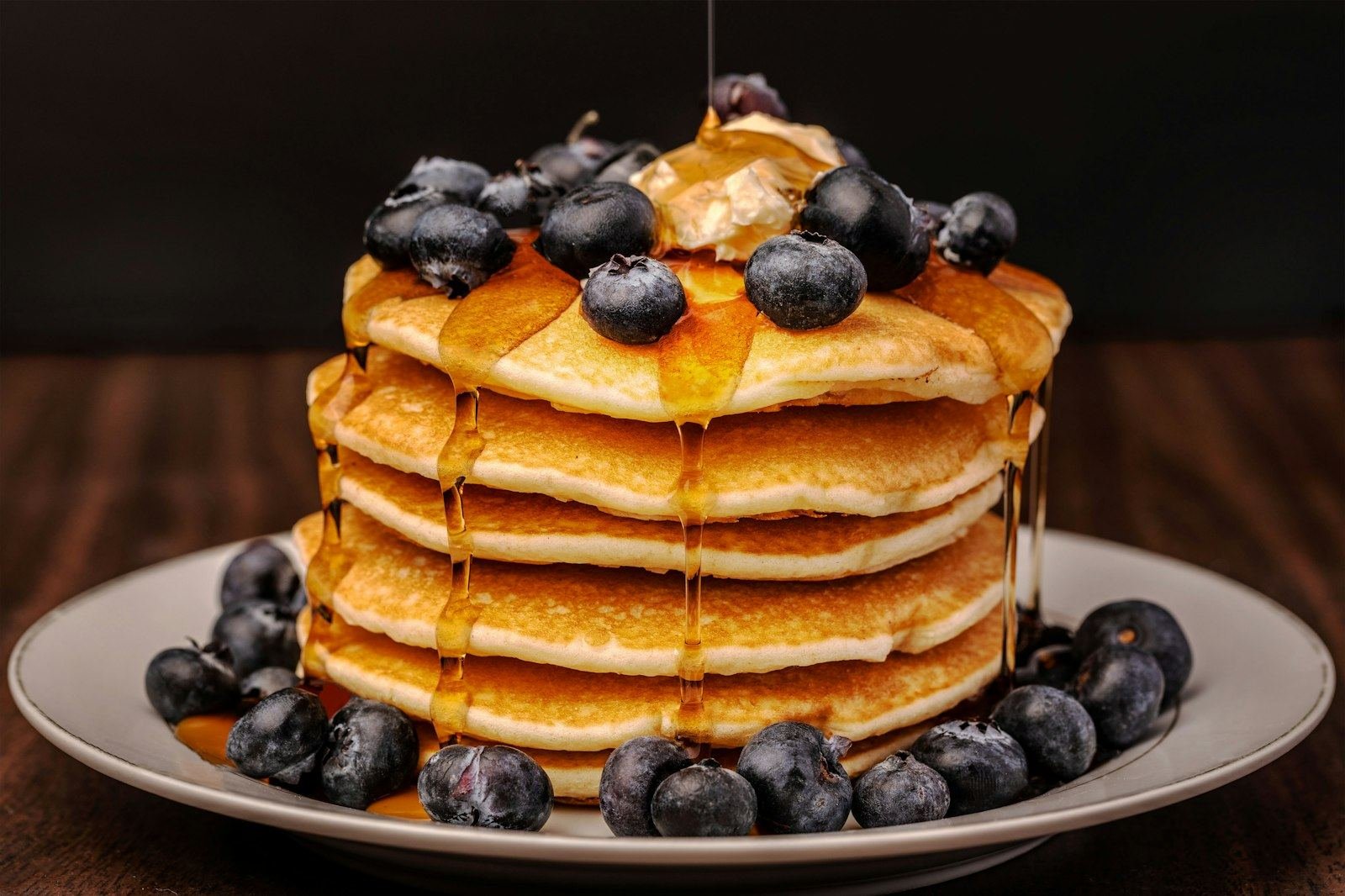 A tall stack of golden buttermilk pancakes topped with blueberries and syrup