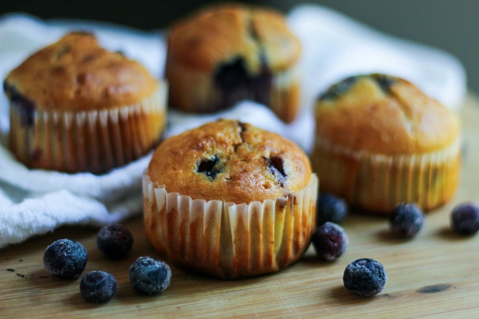 Golden blueberry muffins in paper liners on a wooden table with fresh blueberries
