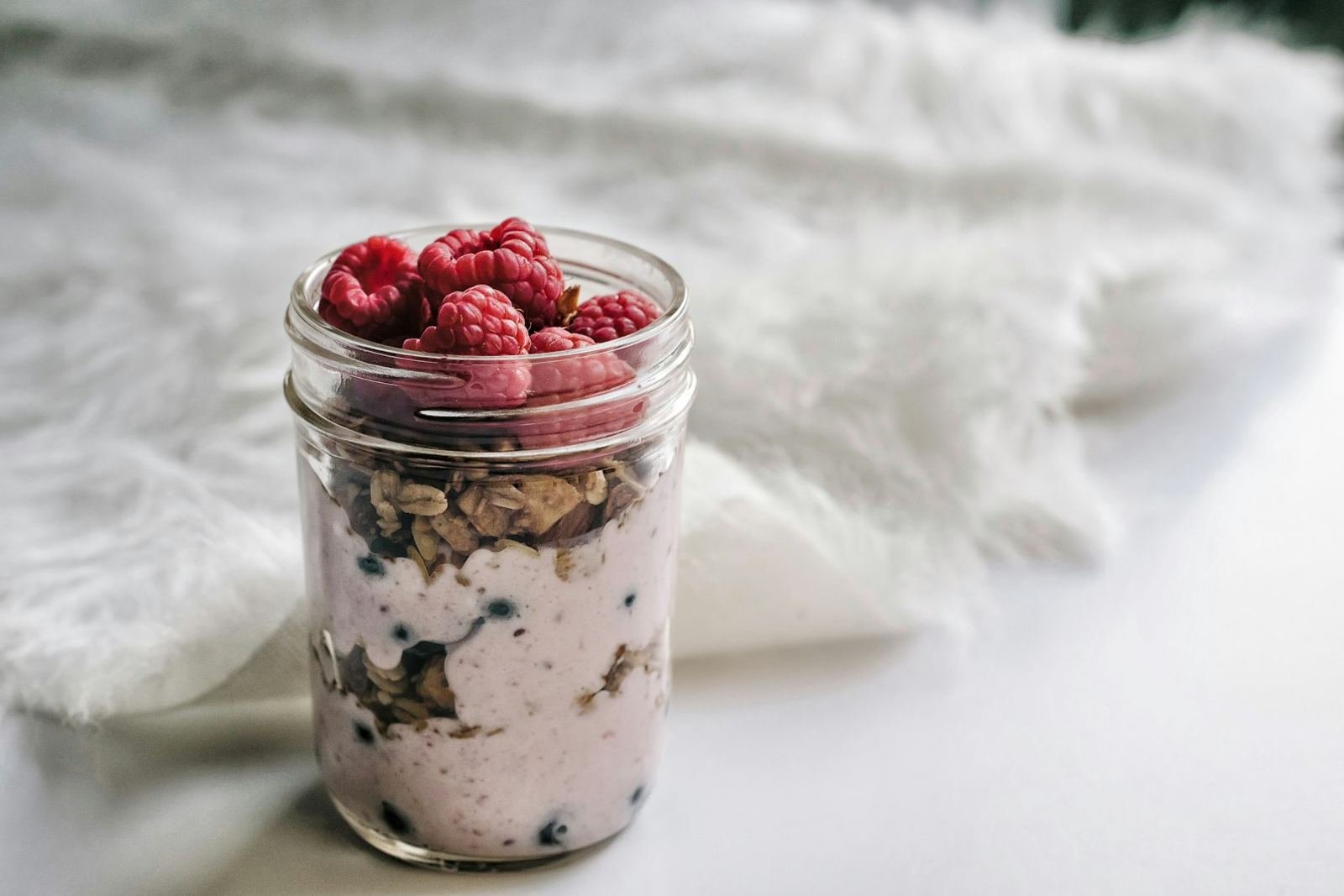 A mason jar of overnight oats layered with yogurt and raspberries