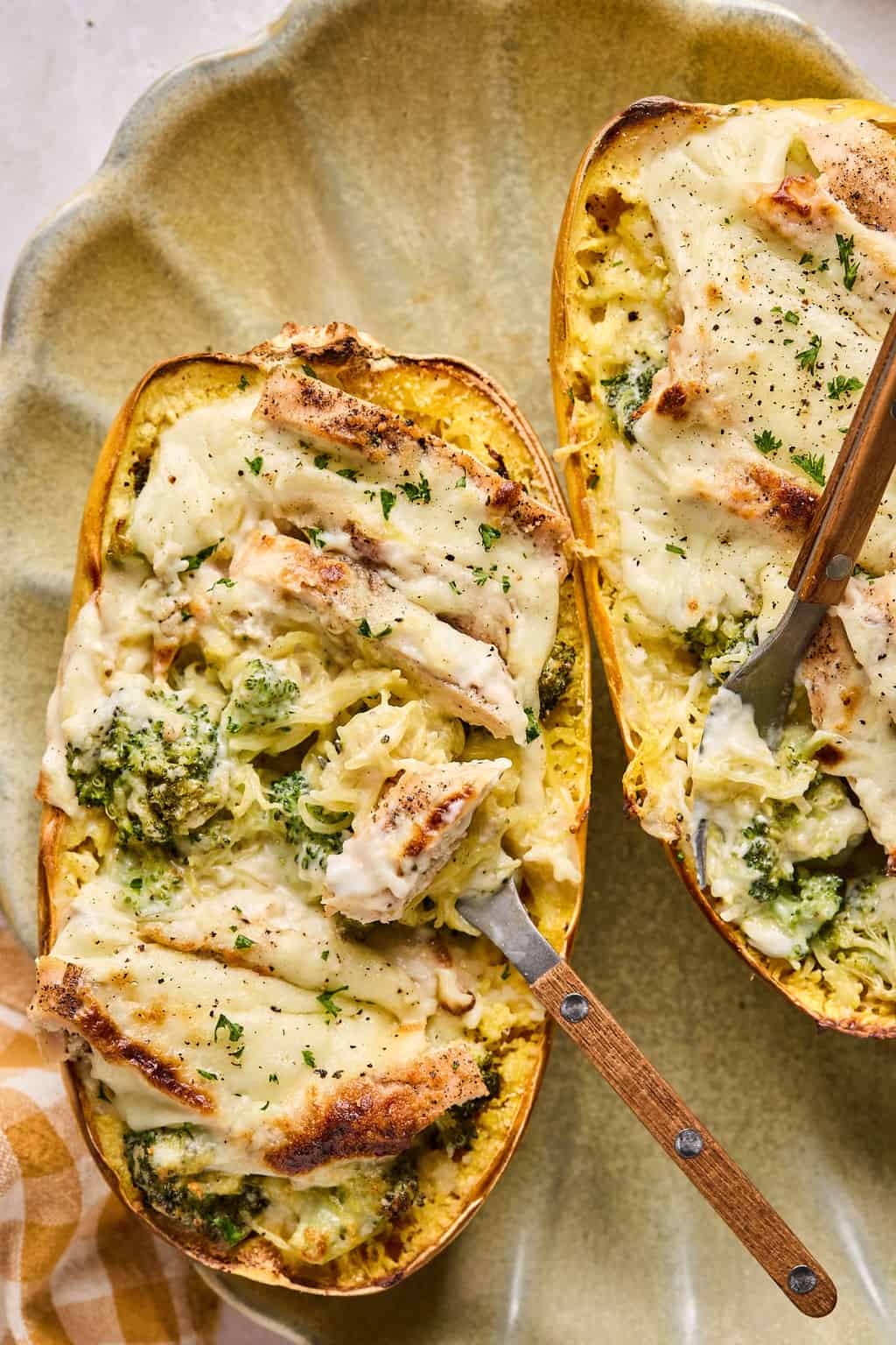 two chicken alfredo spaghetti squash boats on a scalloped plate with a fork.