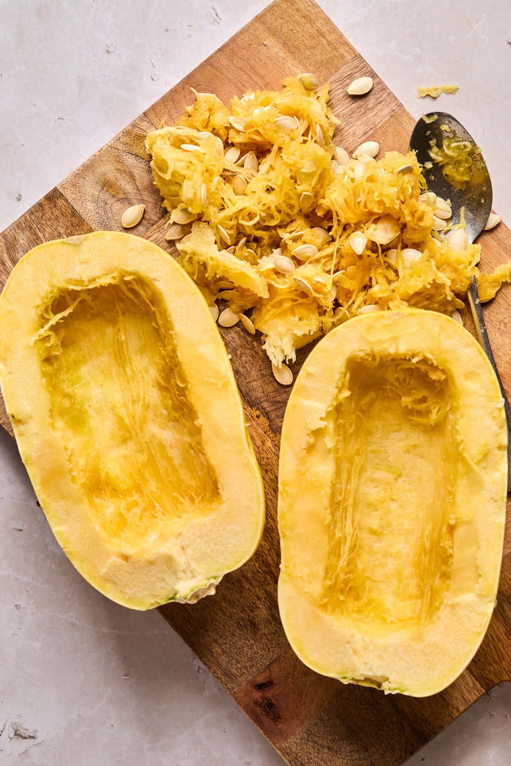 spaghett squash cut in half on a cutting board with the seedy centers scooped out.